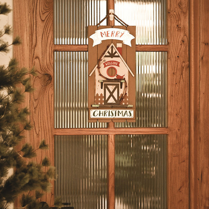 Decorative Christmas sign with a barn design hanging on a wooden door.