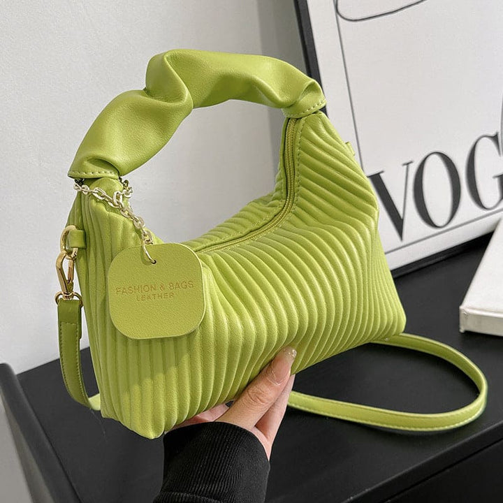 Green pleated handbag held by a hand with a 'Fashion & Bags' tag, placed on a surface with a 'Vogue' magazine in the background.