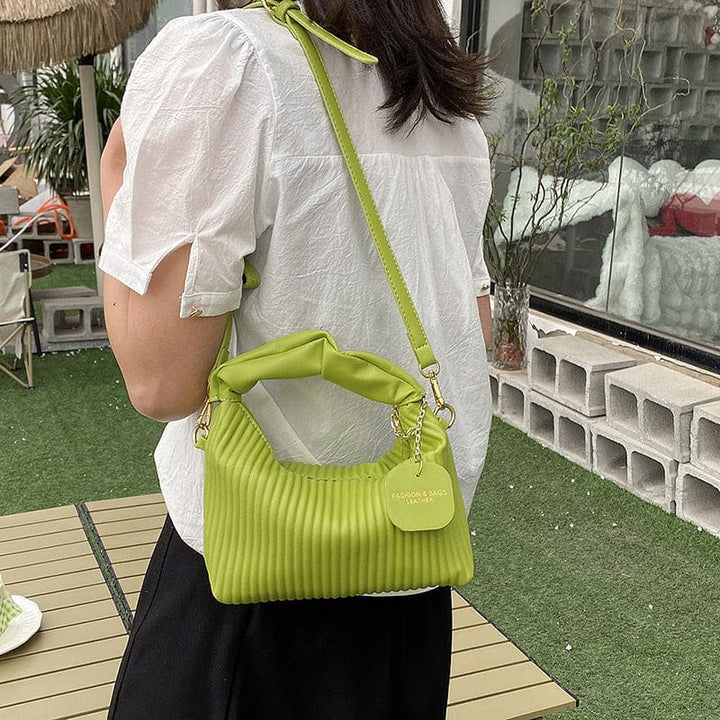 Person wearing a white shirt and holding a green handbag in an outdoor setting.