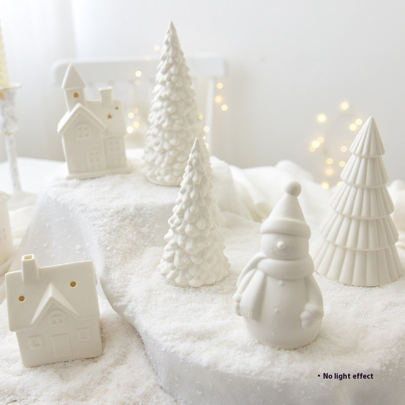 White ceramic Christmas trees and snowman on a snowy surface with a soft white background.