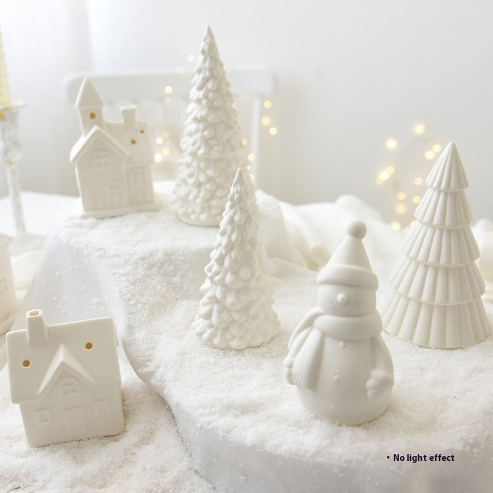 White ceramic Christmas trees and snowman on a snowy surface with a soft white background.