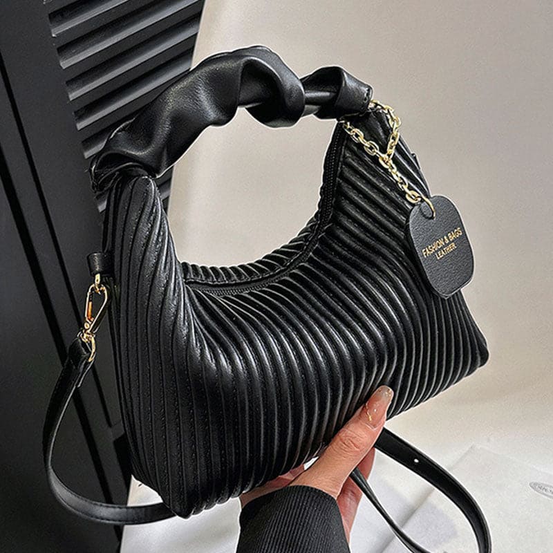 Black pleated handbag held by a hand with a blurred background