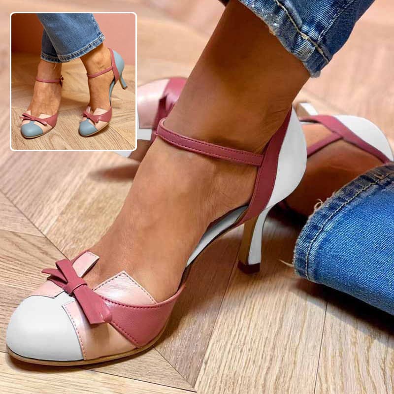 Pink and white high-heeled shoes with a bow detail worn by a person on a wooden floor.