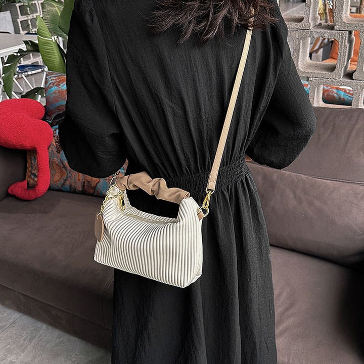 Person wearing a black dress holding a white textured handbag in an indoor setting.
