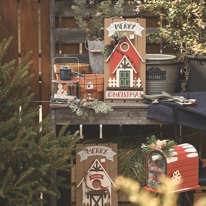 Decorative Christmas signs and mailbox on a wooden surface with greenery.