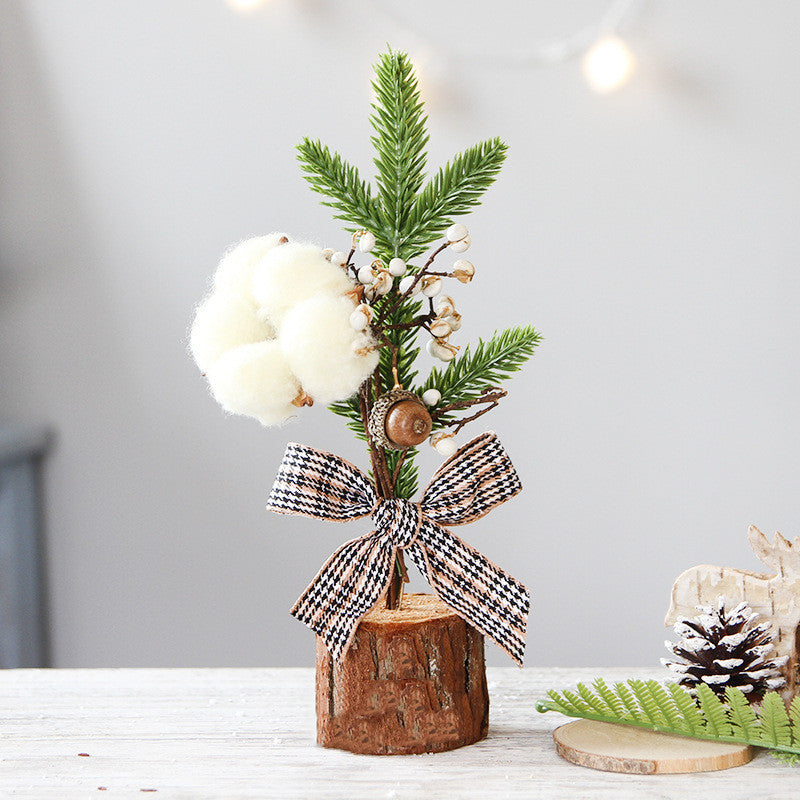 Decorative arrangement with greenery, cotton, and a bow on a wooden base against a light background