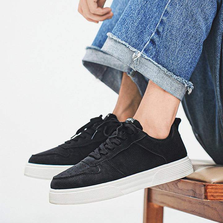 Black sneakers with white soles worn with blue jeans on a light background