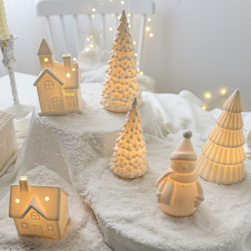 Decorative winter scene with ceramic trees, houses, and a snowman on a white surface.