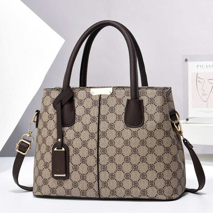 Patterned beige brown handbag with brown handles and strap on a light gray background
