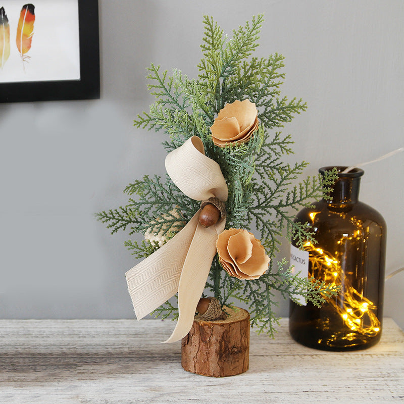 Decorative arrangement with greenery, flowers, and a ribbon on a wooden base, next to a lit brown bottle.