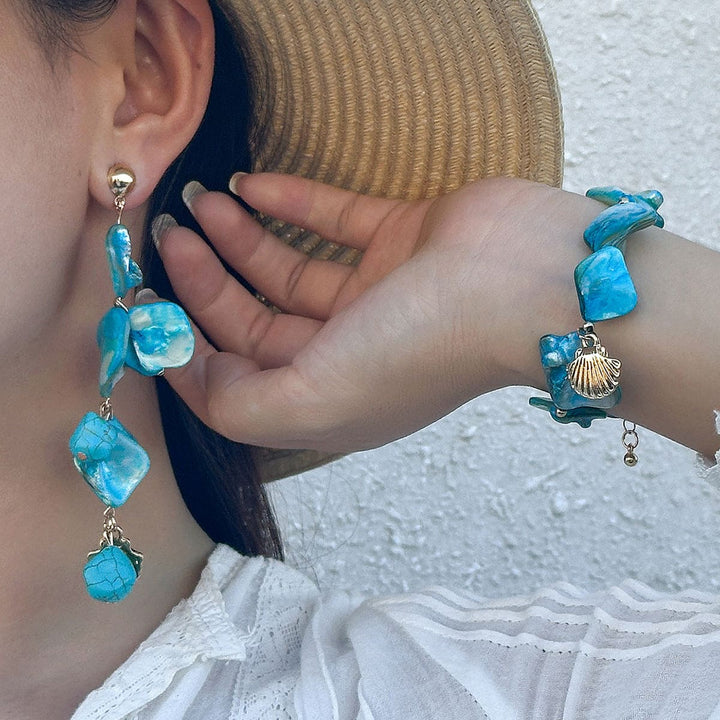 Close-up of turquoise earrings and bracelet worn by a person.
