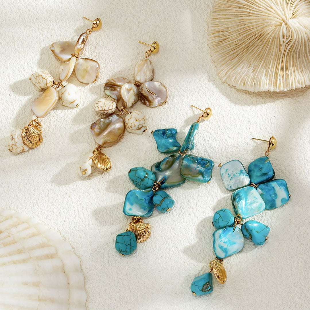 Pair of turquoise stone earrings with gold accents on a sandy background with seashells.