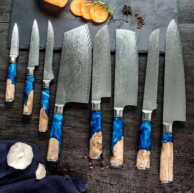 Set of 8 Japanese professional kitchen knives with 9cm Paring knife, 12cm Universal knif1, 5cm Boning knife, 19cm Cleaver, 20cm Chef knife, 20cm Nakiri knife, 19cm Bread knife, and 24cm Chef knife on a reflective wooden background with slate board
